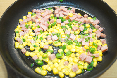 На сковороде разогреть растительное масло и обжарить кукурузу, лук и ветчину.