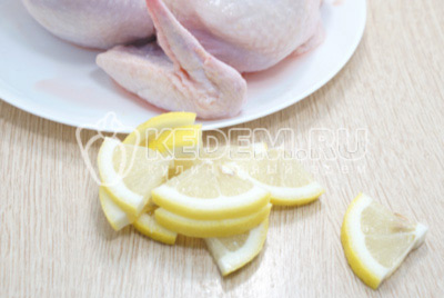 Лимон нарезать ломтиками и вложить внутрь курицы.