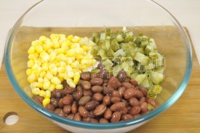 Добавить в миску 200 грамм консервированной кукурузы и 2 маринованных огурца нарезанных кубиками.